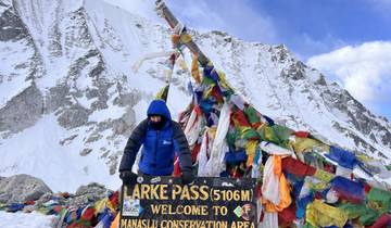 Person at Larke Pass sign with colorful prayer flags and snowy mountain background.