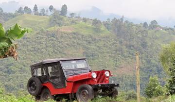 Red Jeep parked in a hilly area with lush greenery