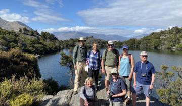 Group of people standing in front of a lake with mountains in the background.