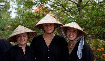 Three people wearing conical hats smiling outdoors.