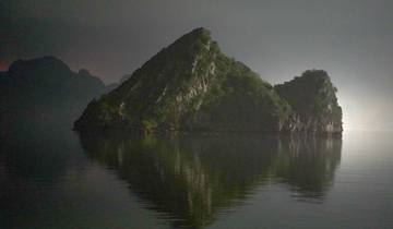 Steep rocky island with reflection in water at night.