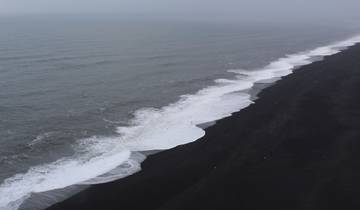 Black sand beach with waves crashing on the shore.
