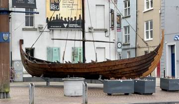 A wooden Viking-style boat displayed in a city square with buildings in the background.