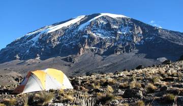A tent in front of a vast mountain landscape under a clear sky.