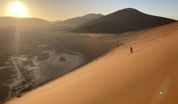 A person walking down a sand dune in the desert with the sun setting.