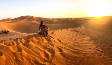 A person sitting on sand dunes during sunset.