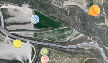Hot air balloons floating over a diverse landscape with fields and roads.