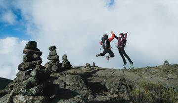 Two people jumping on a rocky mountain trail.