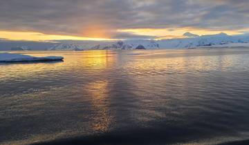 Ocean view with icebergs and a vibrant sunset sky reflecting on the water.