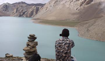 Person sitting by a cairn taking a picture of a glacial lake.