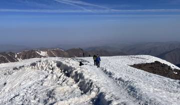 Hikers walking on a snow-covered mountain ridge with a view.