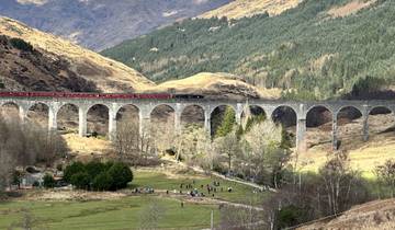 A train crossing a historic viaduct with mountains in the background.