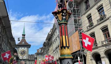 A statue with Swiss flags in a city square with a clock tower.