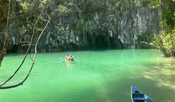 People in a boat heading towards a cave entrance on clear green water.
