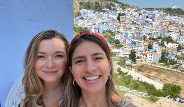 Two people smiling with a background of blue-painted buildings.