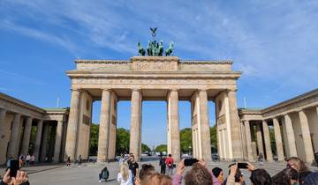 Large historic gate with sculptures on top, surrounded by tourists.