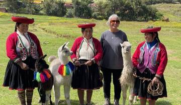 Women in traditional clothing with alpacas in a rural setting.