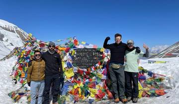 Group of trekkers celebrating at the Thorong La Pass with colorful prayer flags and snow.
