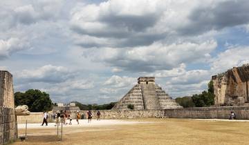The pyramid of Chichen Itza with tourists under a cloudy sky.