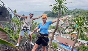 Two people on a zipline with a scenic view of town and ocean.