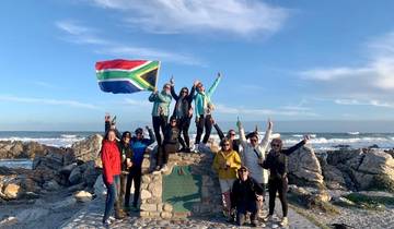 Group celebrating with a South African flag on a rocky shore.