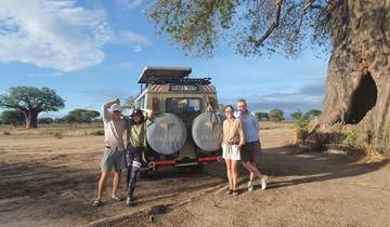 Group of people posing in front of a safari vehicle with a large tree.