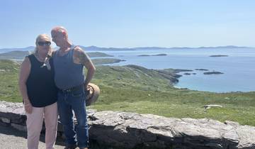 A couple standing in front of a scenic coastal landscape with islands visible in the distance.