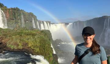 A person smiling in front of a waterfall with a rainbow in the background.