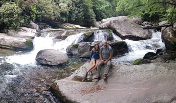 Two people sitting on a rock by a waterfall.