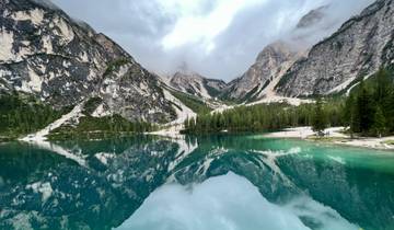 A stunning lake reflecting the surrounding mountains and trees under cloudy skies.