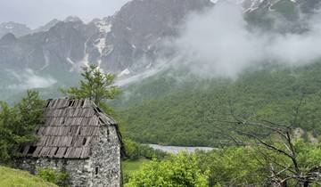 Old stone cabin in front of misty mountains.