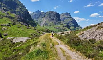 Person walking on a path through tall green mountains.