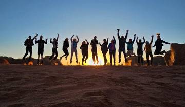 Group of people jumping at sunset in a desert landscape.