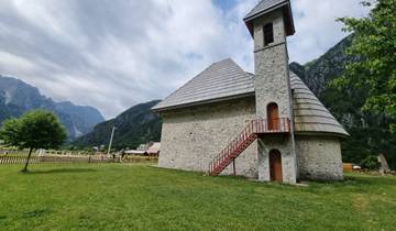 Small stoned church with red stairs in a valley.
