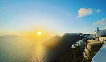 Dramatic sunset over the Aegean Sea with architectural structures on a cliff.