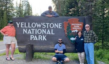 Group posing in front of the Yellowstone National Park sign with trees in the background.