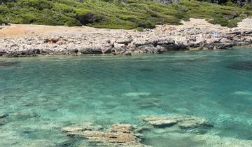 Clear turquoise waters with rocky shoreline and green vegetation.
