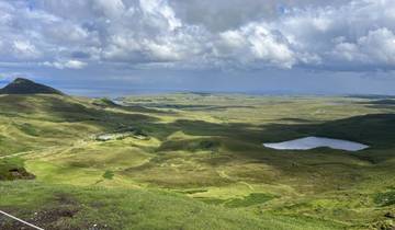 Rolling green hills with patches of water bodies under a cloudy sky.