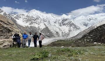 Group of people standing on grass with snowy mountains in the background.
