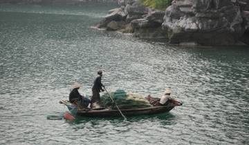 Three people rowing a small boat in a calm river surrounded by rocks.