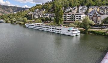 Large cruise ship docked on a river with colorful houses nearby.
