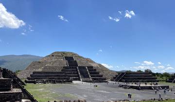 Stepped pyramid with people around, under a blue sky.