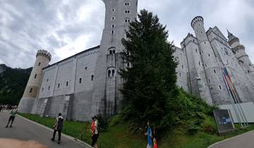 A large stone castle with towers and flags. People are visible along the path.
