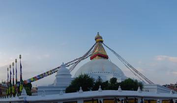 The Baudhanāth Stupa with prayer flags under a clear blue sky.