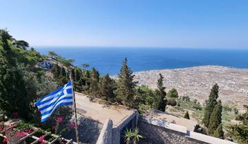 Panoramic view over a coastline with a Greek flag in the foreground.