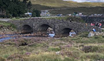 Old stone bridge over a lively stream with people and cars nearby.