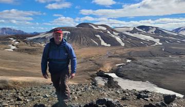 Person hiking on volcanic terrain with snow patches.