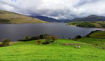 Scenic view of a lake surrounded by rolling hills and clouds.