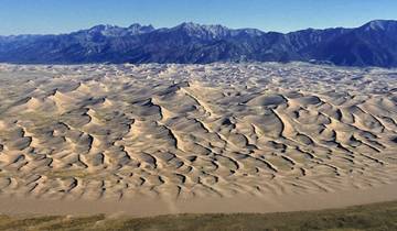 Expansive view of sand dunes with a mountain range in the background.