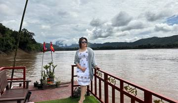 Woman posing on a boat with river and mountains in the background.